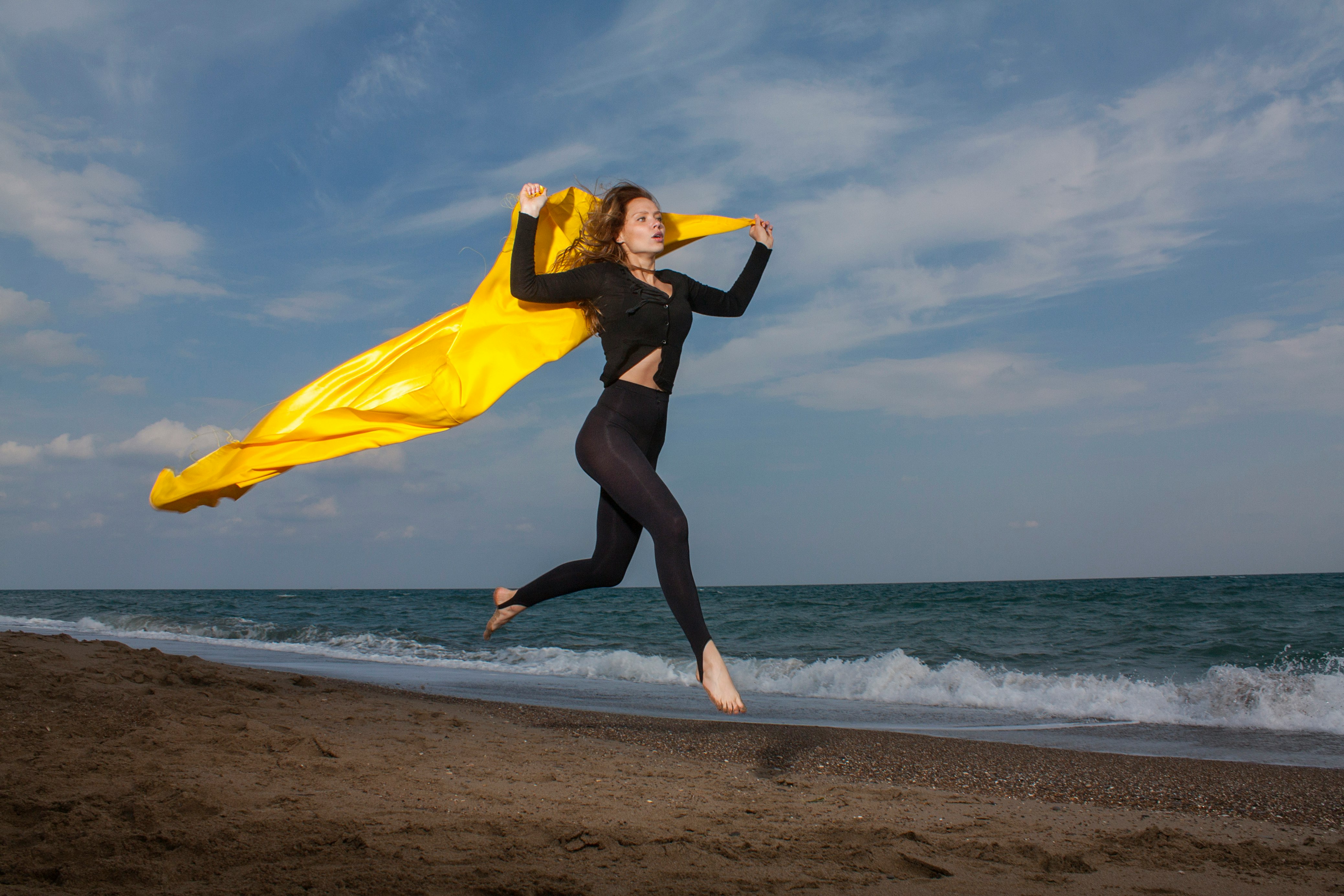 woman in yellow shirt and black leggings holding yellow textile on beach during daytime